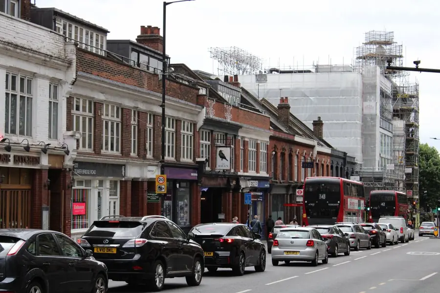 A busy south London road with buses, parked cars and a scaffolded building in the distance