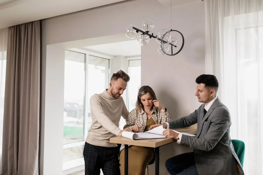 Couple at a table reviewing paperwork with an adviser in a bright room