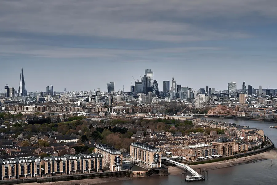 View over riverside housing and the Thames towards the City of London skyline under grey cloud