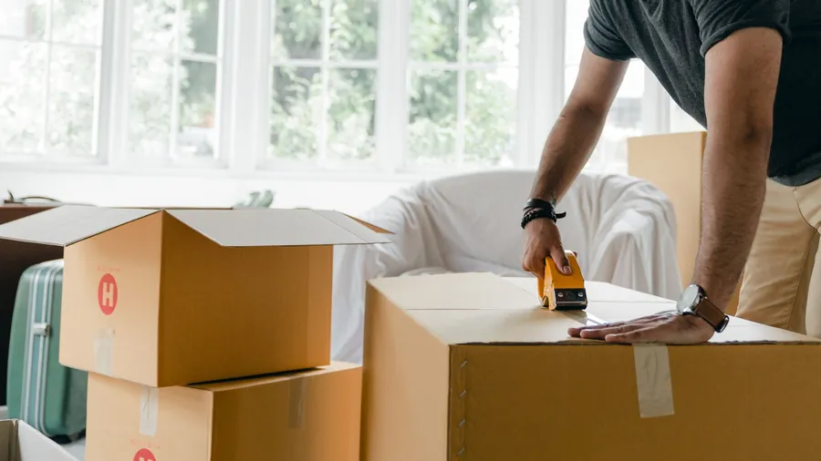 Person taping up cardboard moving boxes in a bright living room