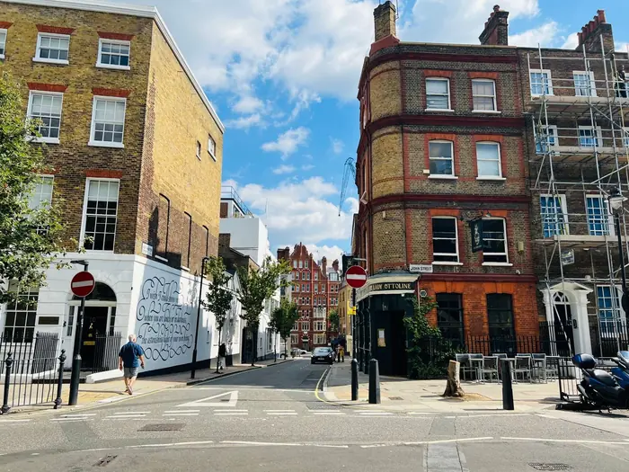 Scaffolding up the front of a brick terrace on a London street corner, standing on the pavement