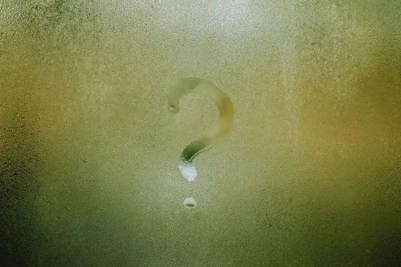 A question mark drawn with a finger in condensation on a misted pane of glass