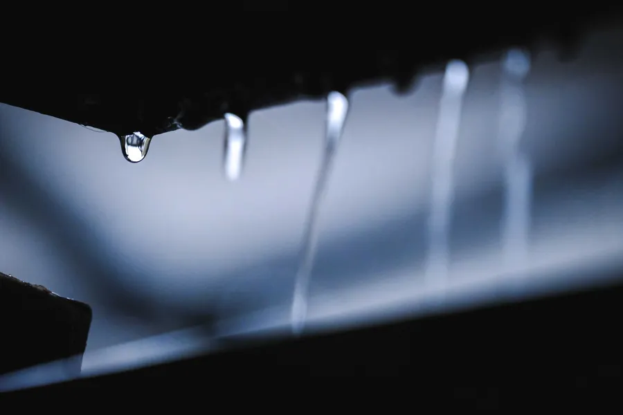Close-up of rainwater dripping from a dark roof edge