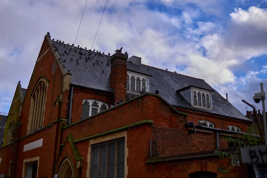Red brick Victorian hall with a steep slate roof, dormers and a tall chimney