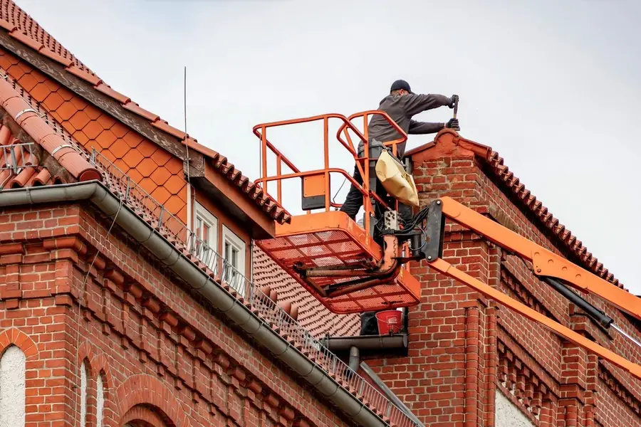 A roofer working from an access platform against a red brick Croydon house