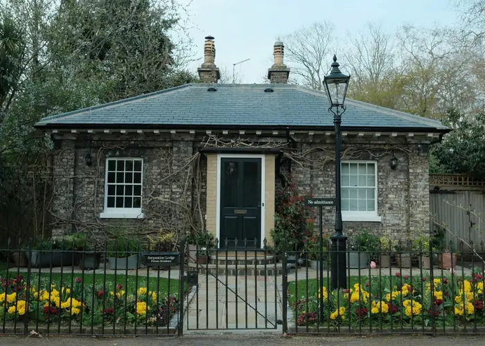 A single storey brick house with a low hipped slate roof and two chimneys behind railings