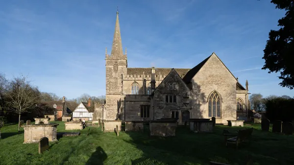 Old English stone church with a spire and a churchyard of weathered gravestones
