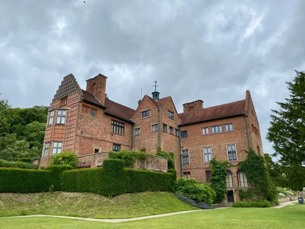 Large red brick country house with tall chimneys and gables above a lawn