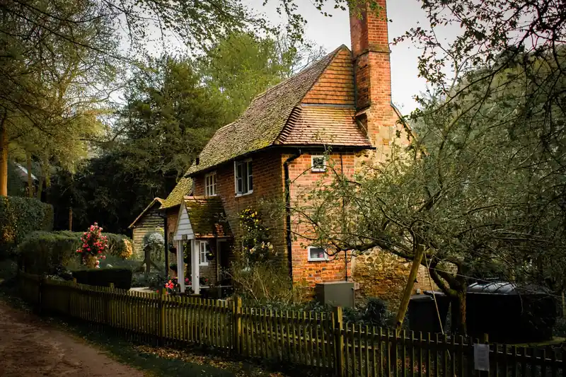 Brick cottage with a steep tiled roof and tall chimney in a cottage garden
