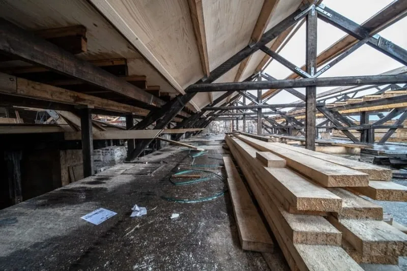 Large roof space with dark timber trusses overhead and stacks of new sawn timber laid on the floor